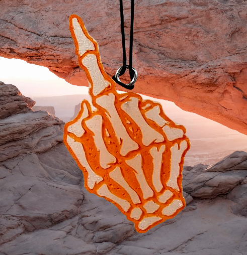 Orange middle-finger skeleton hand freshie against desert rock